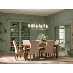 a dining room with green walls and wooden table surrounded by beige upholstered chairs