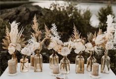 there are many vases with flowers and feathers in them on the white table cloth