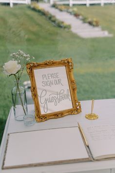 a sign that says please sign our guest book on a table next to a vase with flowers