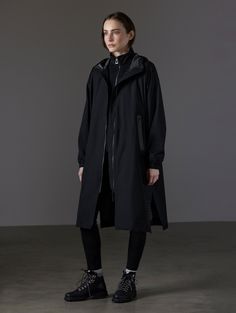 Front angled full-body view of woman wearing Kite Packable Rain Poncho in Onyx Black from AETHER Apparel. Black Windproof Raincoat For Rainy Season, Functional Black Raincoat For Rainy Season, Black Functional Raincoat For Rainy Season, Black Functional Raincoat, Oversized Black Waterproof Outerwear, Functional Black Windbreaker For Rainy Season, Black Windproof Outerwear For Rainy Season, Oversized Black Waterproof Raincoat, Oversized Black Raincoat