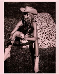 a woman sitting on top of a rug wearing a cowboy hat and holding her leg