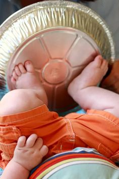 a baby laying on top of a bed next to a metal pan