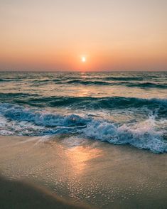 the sun is setting over the ocean with waves crashing on the beach and sand in front of it