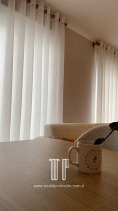 a coffee cup sitting on top of a wooden table next to a curtained window