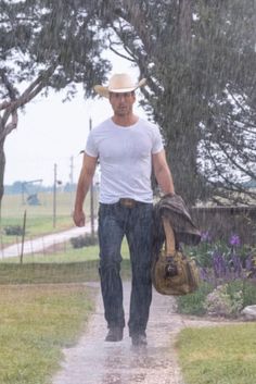 a man walking in the rain with his hat on and bag under his arm,