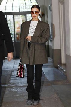 a woman walking down a hallway carrying a handbag in her right hand and wearing sunglasses