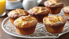 some muffins are on a cooling rack with orange juice in the back ground