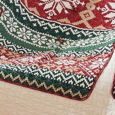 a quilted blanket is laying on top of a bed with red, green and white patterns