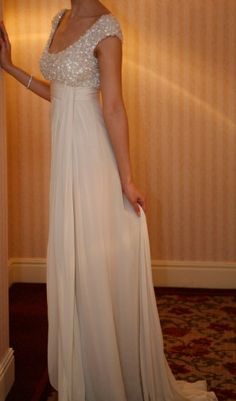 a woman in a long white dress standing next to a wall with her hand on the door