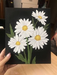 a person holding up a card with daisies painted on it