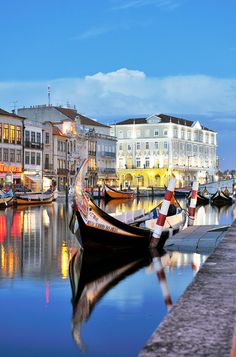 boats are docked in the water next to buildings and lights at night, with blue skies above them