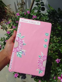 a hand holding a pink notebook with flowers on it