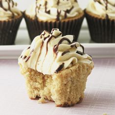 cupcakes with white frosting and chocolate drizzled on top sitting on a plate