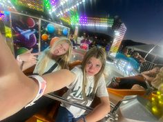 two girls are riding on a roller coaster at the amusement park with lights in the background