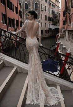 a woman in a dress standing on some steps near buildings and boats with her back to the camera