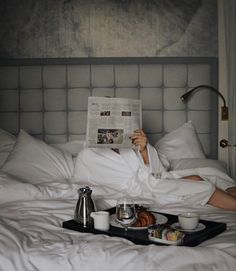 a person laying in bed reading a newspaper and having breakfast on the tray with coffee