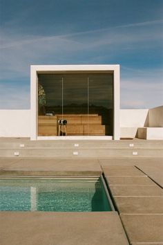 an empty swimming pool in front of a white building with open doors on the side