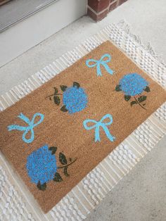 a brown door mat with blue flowers and bows on the front porch, next to a brick wall