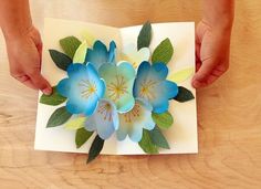 two hands are holding an origami flower on top of a piece of paper