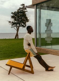 a man sitting on top of a wooden chair in front of a large glass window