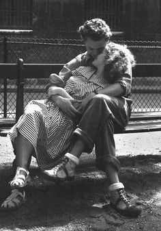 a man and woman sitting on a bench in front of a fence with their arms around each other