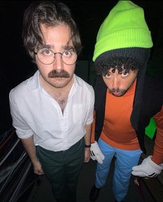 two men wearing beanies and glasses are standing next to each other in the dark