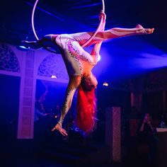 a woman doing aerial acrobatic tricks on a hoop in the middle of a performance