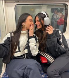 two women sitting on a subway train, one with headphones and the other listening to music