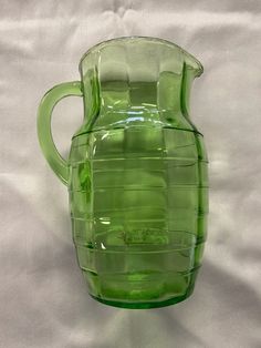 a green pitcher sitting on top of a white sheet