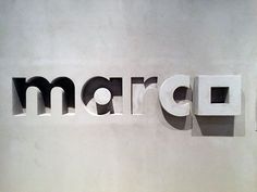 the word marc written in cutout letters on a white wall next to a clock