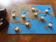 a blue board game with wooden blocks in the shape of boats on water and sand