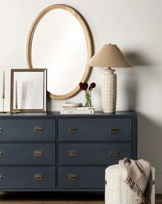 a dresser with a mirror, vase and pictures on it next to a lamp in a room