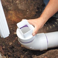 a person is holding a plastic container in their hand while laying on the ground next to a pipe