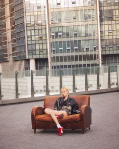 a woman sitting on top of a brown couch in front of tall buildings with her legs crossed