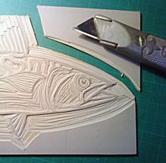 a pair of scissors next to some cut out fish shapes on a cutting board with paper