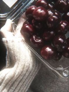 a person's hand holding a container full of cherries next to a pair of gloves