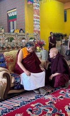 two monks sitting on a couch in a room with other people standing around and looking at them