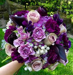 a bride's bouquet with purple and white flowers in her hand on the grass