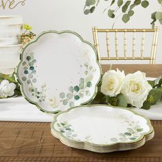 white roses and greenery are sitting on the table next to plates with gold rims