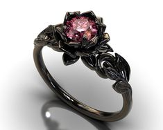 "If you're looking for an engagement ring like no other, stop right here. This AMAZING piece of fine jewelry is the perfect expression of your eternal love. Its BLACK colors bring out the beauty of this ring. This engagement ring is created of gleaming, 14kt black gold, carved into an elaborate leaf design at the top. A striking Pink Sapphire sits boldly at the center, surrounded by black gold petals, forming the eye-catching image of a lotus flower. Item Specifics: (1 Ring Only) Gem Details: Ce Pink And Black Engagement Ring, Black And Pink Wedding Rings, Elegant Black Flower Ring For Wedding, Elegant Black Flower Promise Ring, Elegant Black Flower Ring, Black Sapphire Ring With Brilliant Cut As Gift, Black Sapphire Ring With Brilliant Cut For Gift, Gift Black Sapphire Ring With Brilliant Cut, Elegant Black Flower Ring For Anniversary