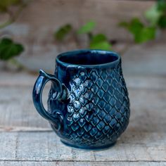 a blue ceramic mug sitting on top of a wooden table next to green leaves and ivy