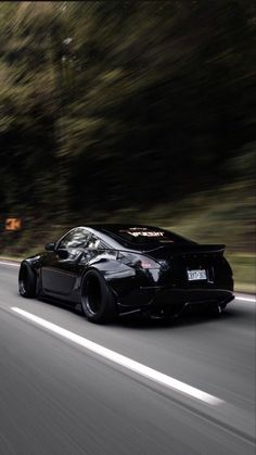 the black sports car is driving down the road with trees in the backgroud