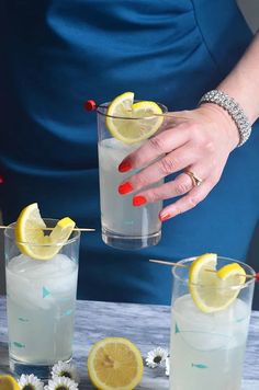 a woman holding a glass with lemons and water in it next to two glasses