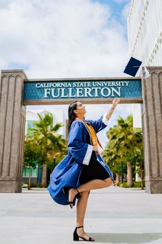 a woman in a blue graduation gown is throwing her cap into the air while standing outside california state university