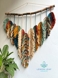 a wall hanging made out of different colors of yarn and feathers with a plant in the corner