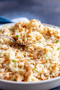 a white bowl filled with rice on top of a blue table cloth and silver spoon