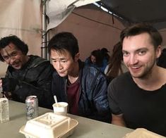 three men sitting at a table with drinks and food in front of them, smiling