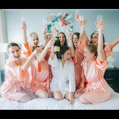 a group of women sitting on top of a bed holding up wine glasses in the air