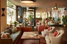 a living room filled with lots of furniture next to a tall glass wall covered in potted plants