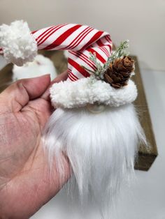 a hand is holding a small white santa clause ornament with a pine cone on top